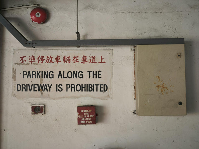 Bilingual parking prohibition sign on an industrial indoor wall with fire safety equipment.