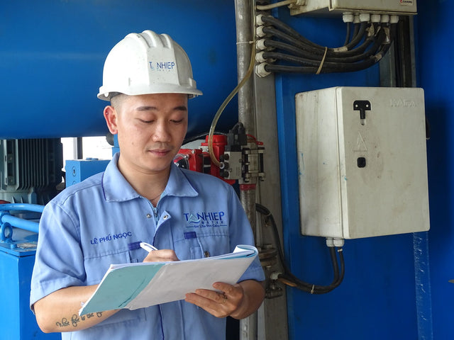Engineer in safety gear inspecting machinery, taking notes indoors at an industrial facility.