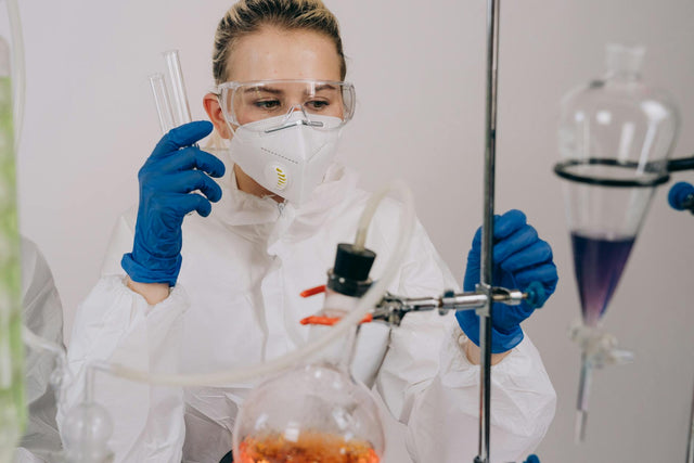 Female scientist in protective gear performing laboratory work with chemicals and equipment.