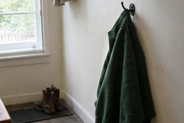 A worn green polyester fleece jacket hanging on an iron hook in a mudroom beside a window. About a third of a polyester fleece’s weight comes from ethylene glycol.
