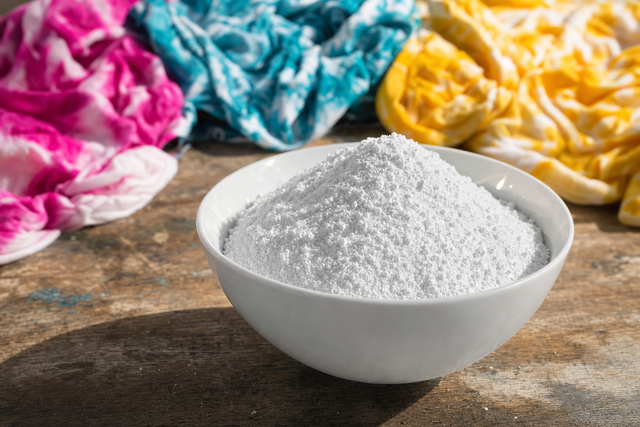 White soda ash powder in a ceramic bowl with vivid tie-dye shirts soft-focused behind