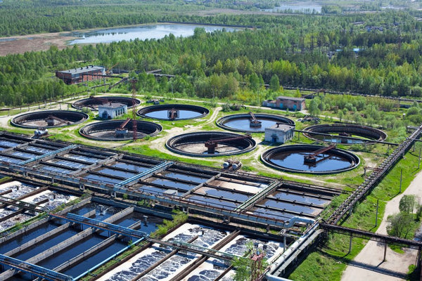 Aerial view of water treatment plant with circular clarifier tanks surrounded by forest