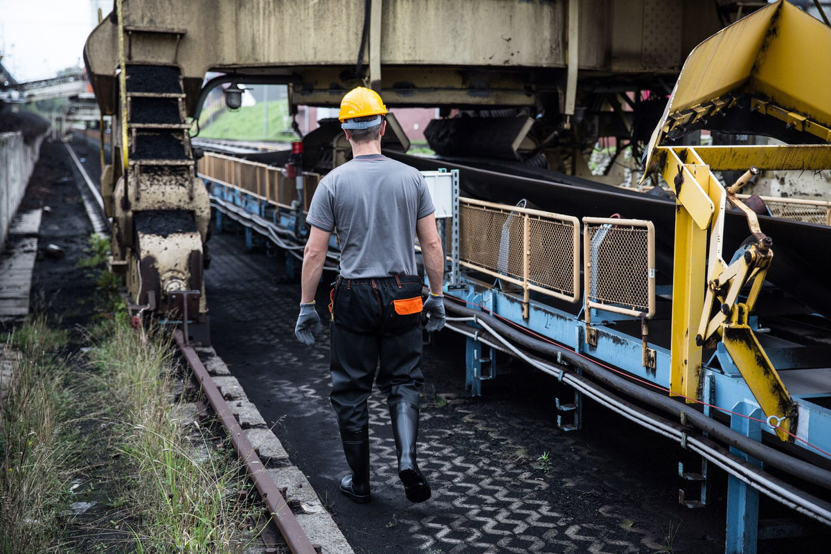 A worker in safety gear examines industrial machinery in an outdoor setting, showcasing industry work.