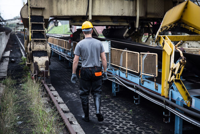 A worker in safety gear examines industrial machinery in an outdoor setting, showcasing industry work.