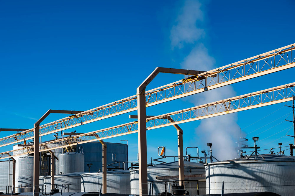 Wide view of an industrial plant with smoke rising from storage tanks against a clear blue sky.