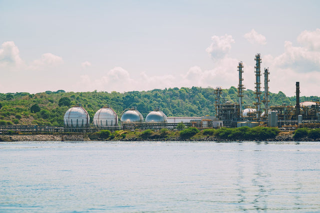 A scenic view of a coastal industrial gas storage facility with spherical tanks and tall chimneys.