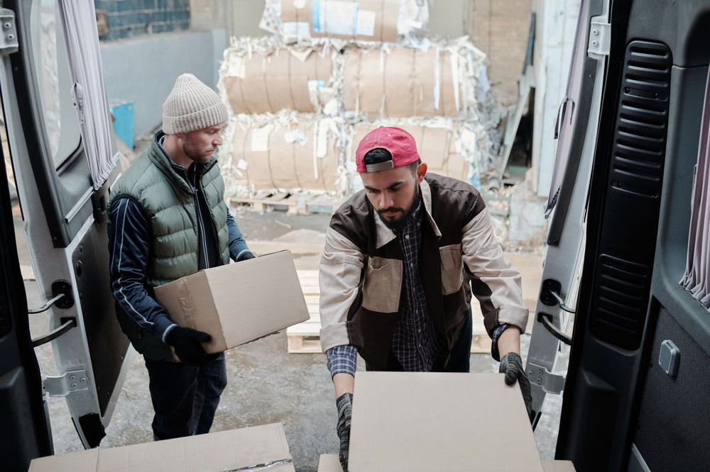 Two delivery workers unloading packages from a van at an industrial site.