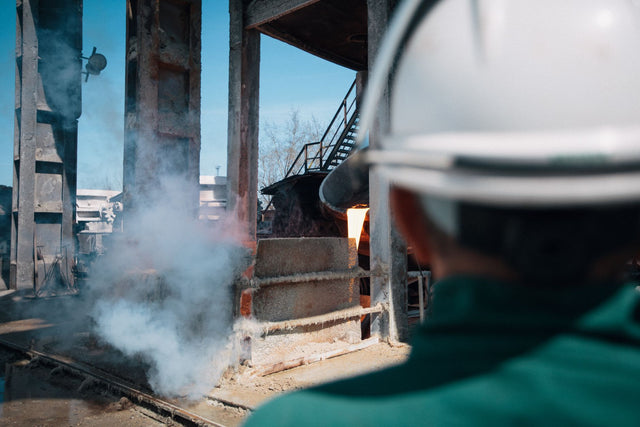 A worker in a hard hat observes a smelting process at an industrial plant.