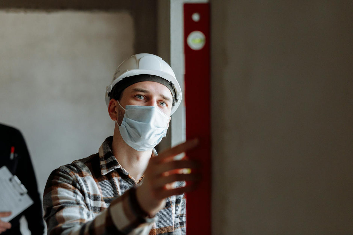 Man wearing a face mask and hard hat conducting safety inspection indoors.