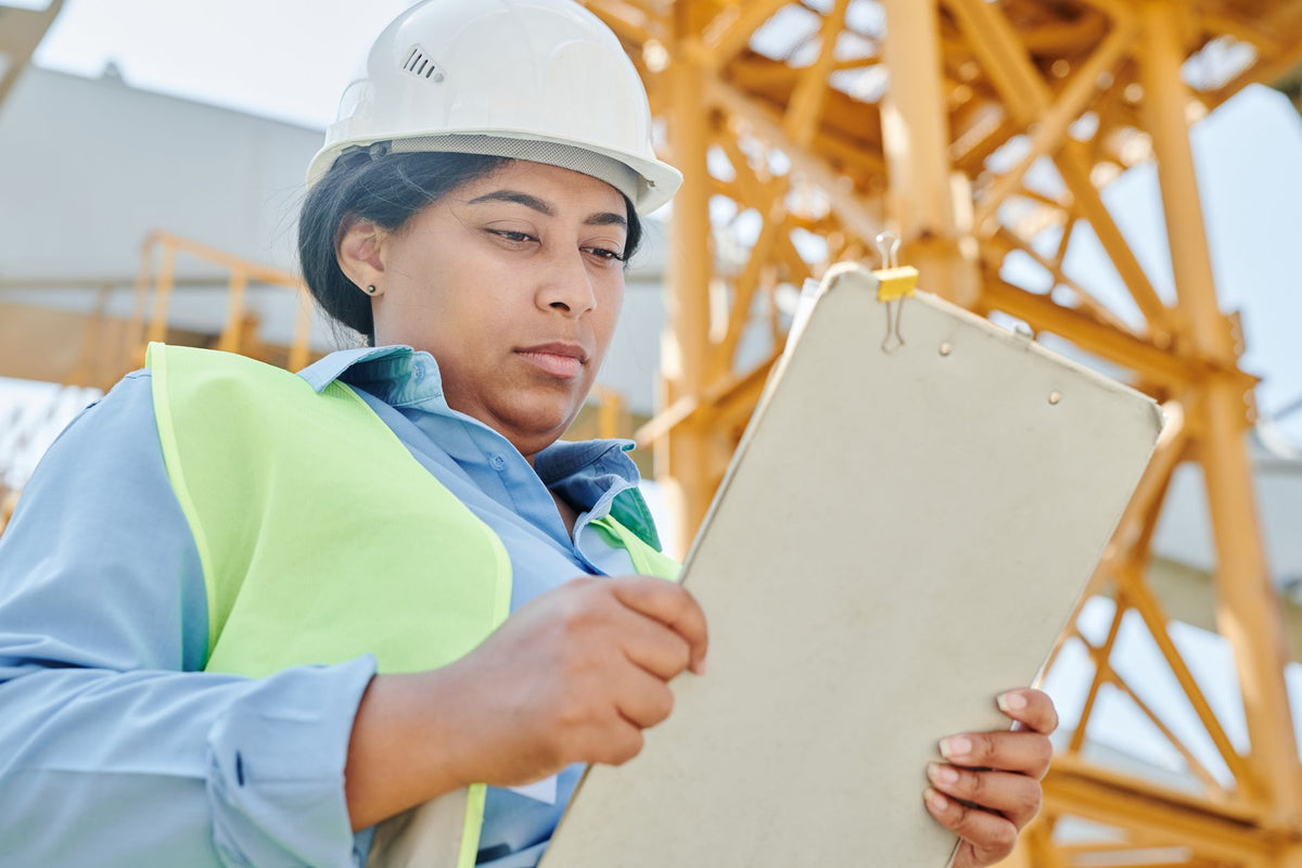 Confident female construction worker inspecting site with clipboard and helmet.