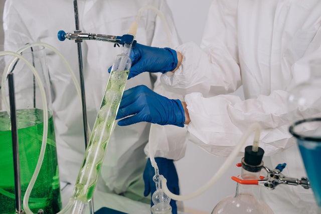 Researchers in protective gear conducting a chemistry experiment with laboratory apparatus.