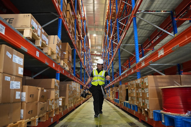 Worker in reflective vest walks through warehouse aisle — workplace safety