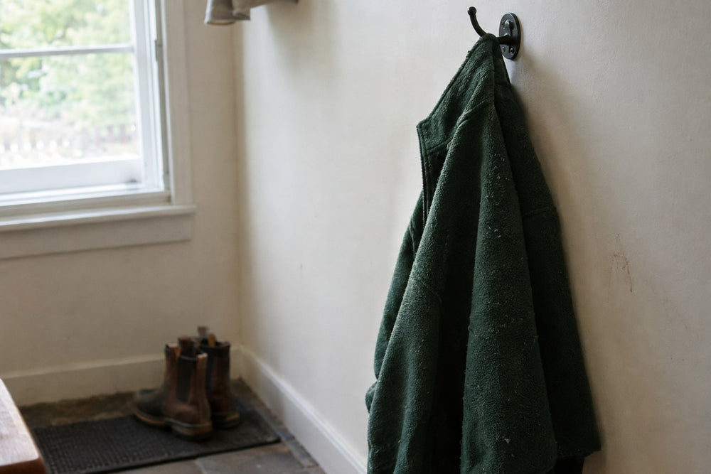 A worn green polyester fleece jacket hanging on an iron hook in a mudroom beside a window. About a third of a polyester fleece’s weight comes from ethylene glycol.
