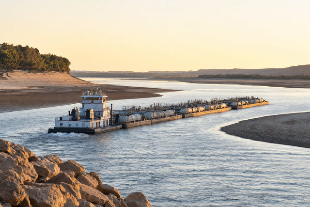 A towboat pushing liquid tank barges down a narrowed river channel with wide sandbars exposed on both sides by record-low water