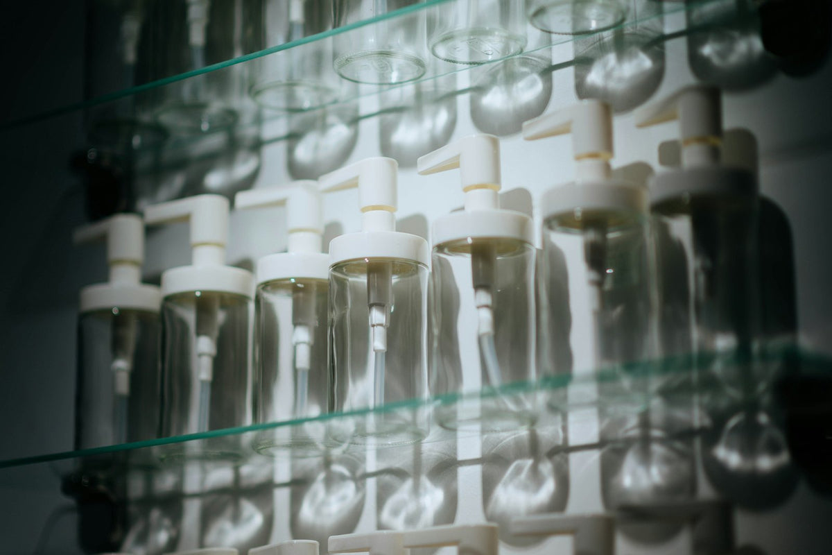 Empty clear bottles with white pump heads lined up on glass shelves