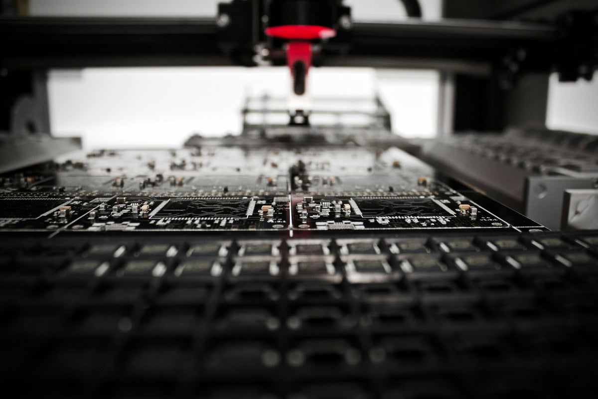 Automated placement head with a red nozzle above panels of black printed circuit boards