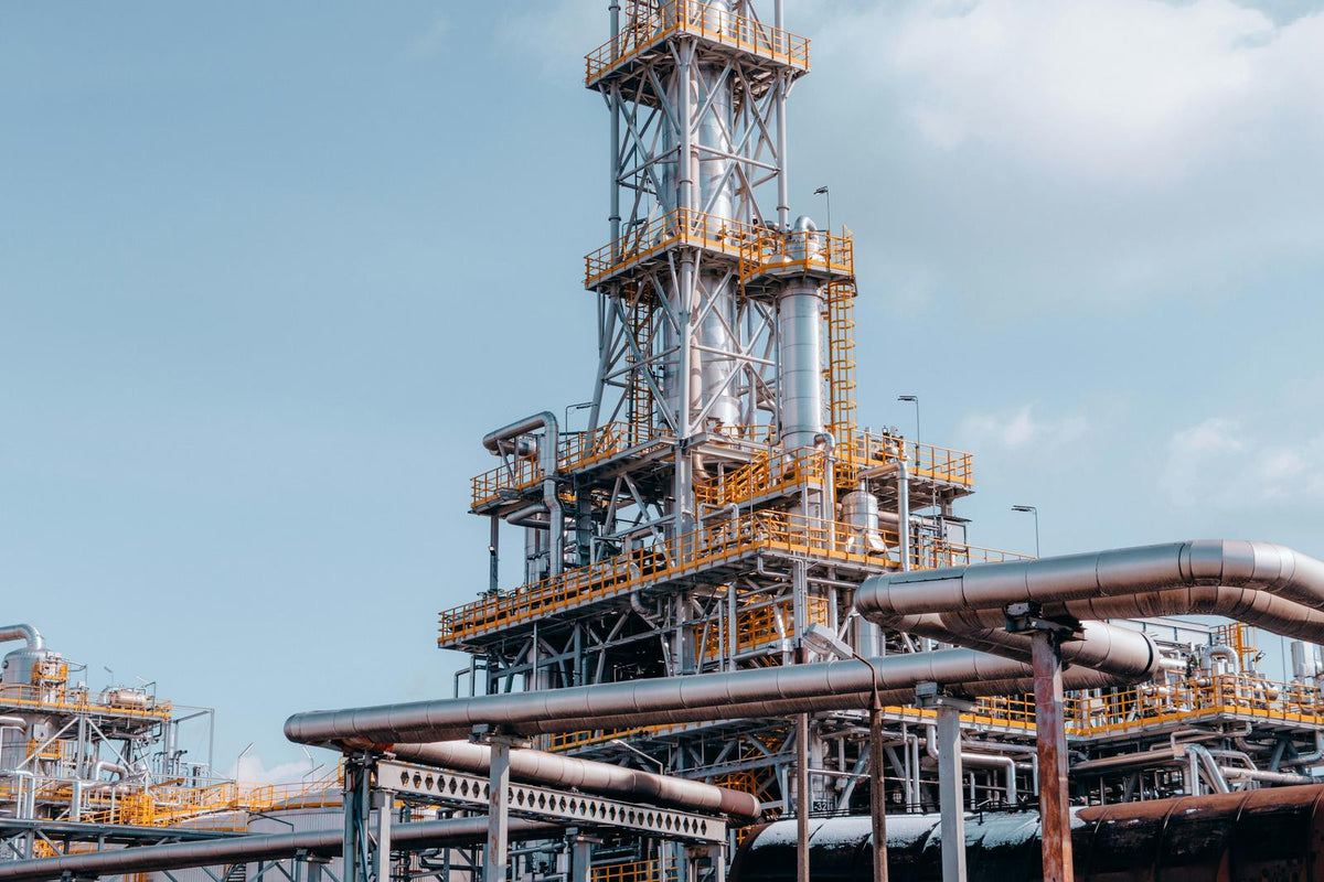 Refinery distillation tower with yellow-railed platforms and insulated pipe racks under a blue sky