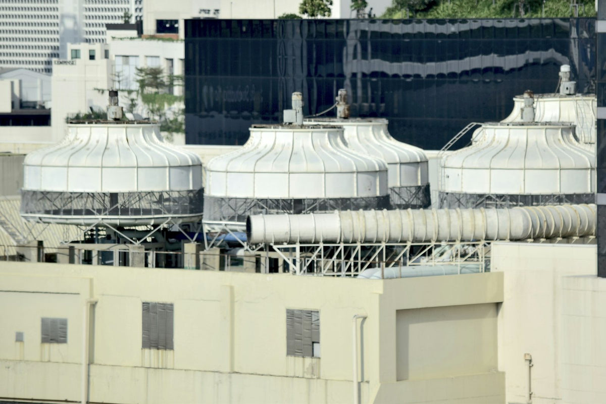 Round white cooling towers and a ventilation duct on a city building rooftop