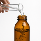 Acetone pouring from a graduated cylinder into an amber lab bottle — Alliance Chemical ACS-grade solvent